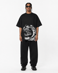 A model wearing a black oversized t-shirt with a large black and white roaring tiger graphic on the front, paired with black sweatpants and black sunglasses, against a plain white studio background.