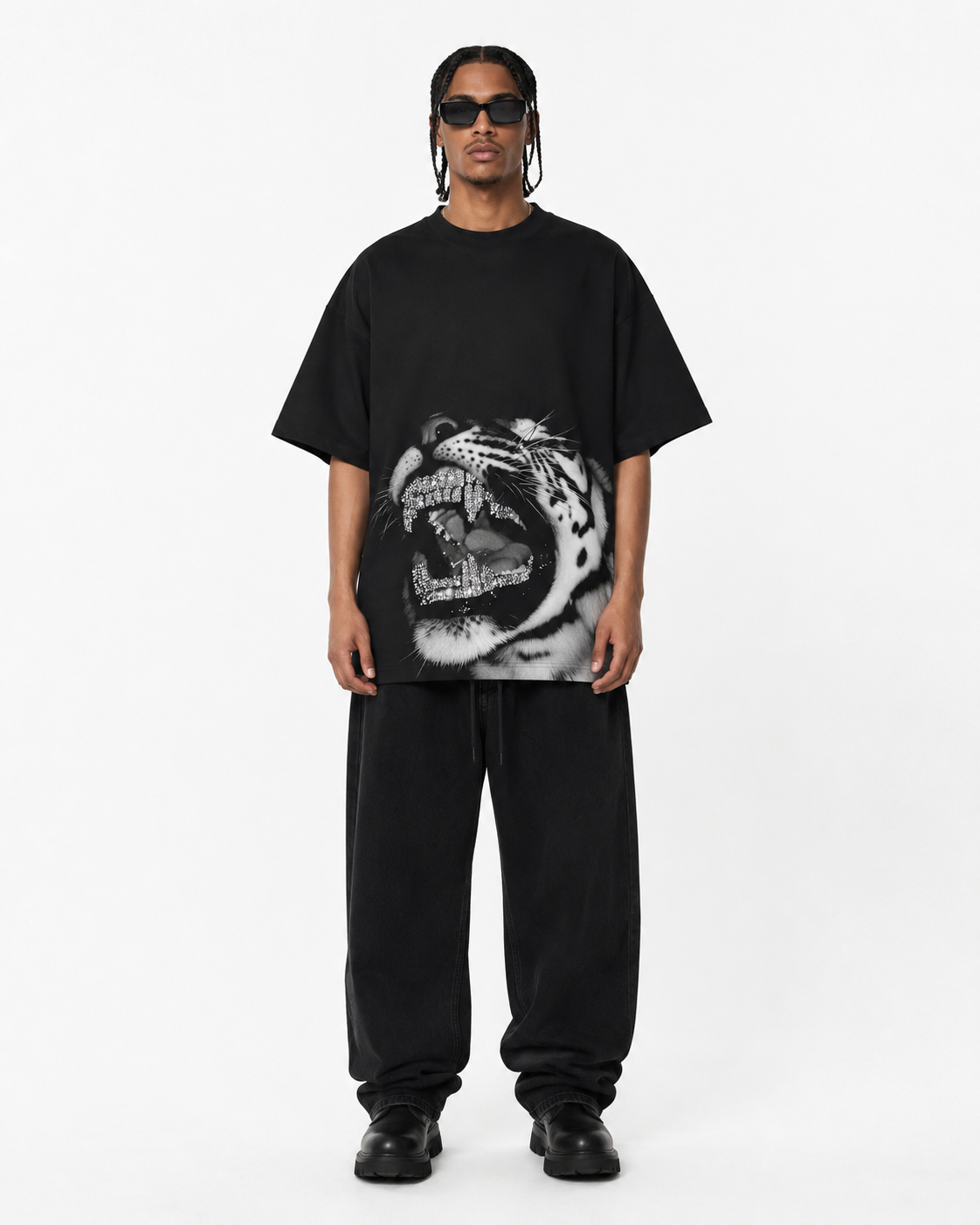 A model wearing a black oversized t-shirt with a large black and white roaring tiger graphic on the front, paired with black sweatpants and black sunglasses, against a plain white studio background.