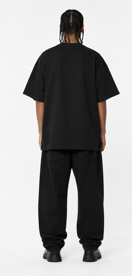 A person shown from the back wearing an oversized black short-sleeve T-shirt and loose black pants against a plain light gray studio background.