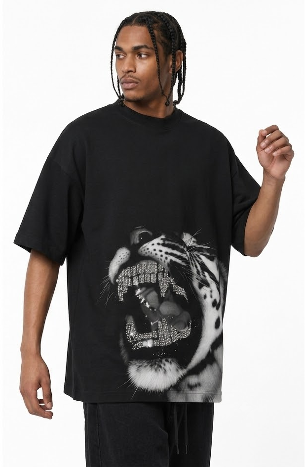 A man wearing a black oversized t-shirt with a large black and white graphic print of a roaring tiger on the front, paired with black pants, against a plain white background.
