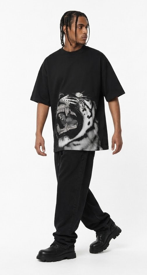 A man modeling an oversized black t-shirt with a large black and white tiger graphic on the front, paired with black pants and black boots, against a plain white studio background.